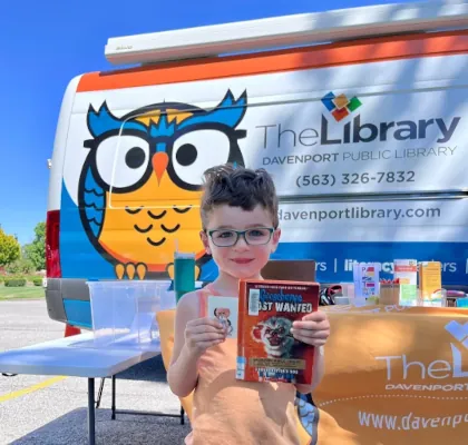 Young patron standing in front of the Outreach Wheeled Library (OWL).